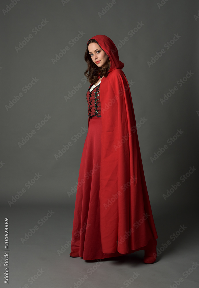 full length portrait of woman wearing red fantasy costume with cloak, standing pose on grey studio background.