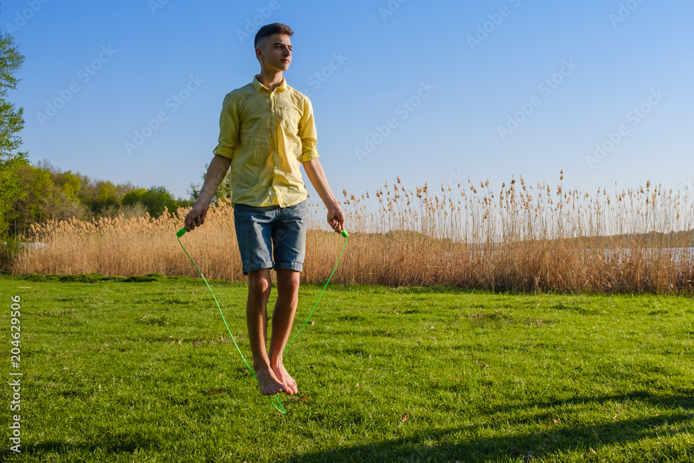 Young caucasian boy is doing workout with jumping rope on green grass lawn