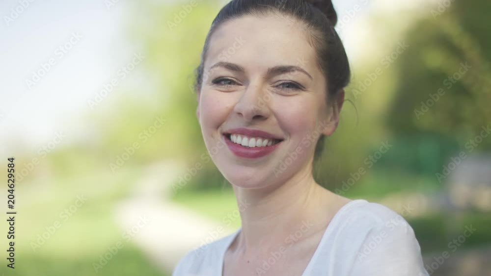 Portrait of smiling beautiful woman standing in summer park and looking at camera Portrait of smiling beautiful woman standing in summer park and looking at camera