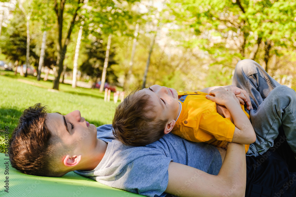 Cheerful two brothers lie on the grass in the park and play in funny games Cheerful two brothers lie on the grass in the park and play in funny games