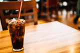 Soft drink with Ice and red straw in glass and blurred woman in background at restaurant