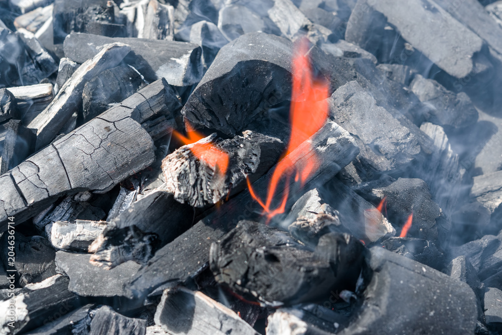 A small smoldering flame of fire on black burned charcoal 
