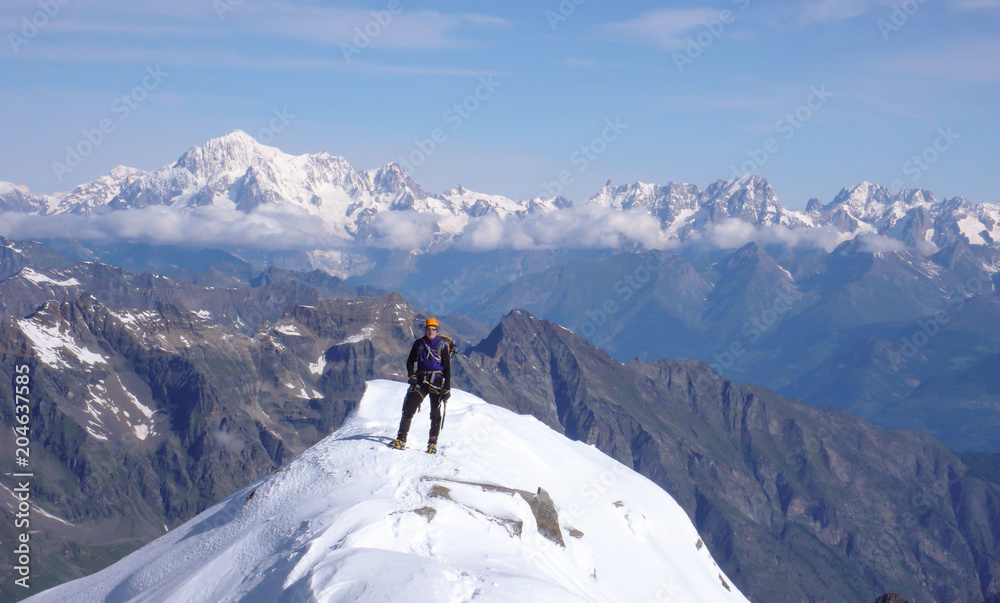 mountain climber on the summit of Gran Paradiso after exiting the north face ascent route with a great view of Mont Blanc behind him