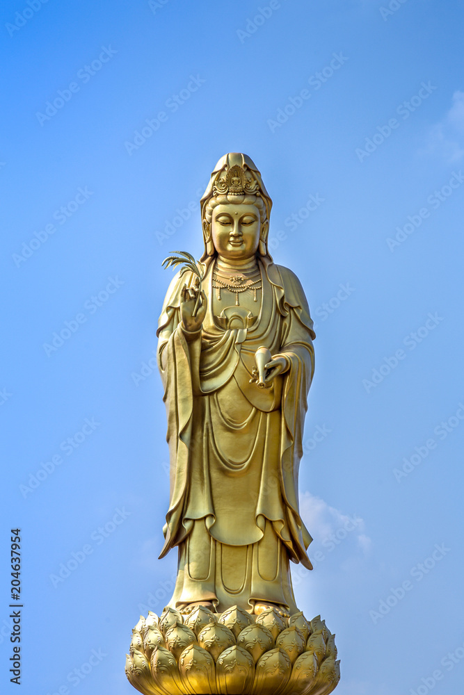 golden statue of the goddess of mercy  guanyin or guan yin standing on the lotus on blue sky background. buddhist and religion concept.