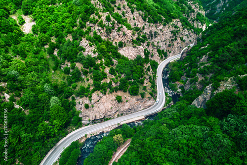 Aerial view  over mountain road and curves going through forest landscape