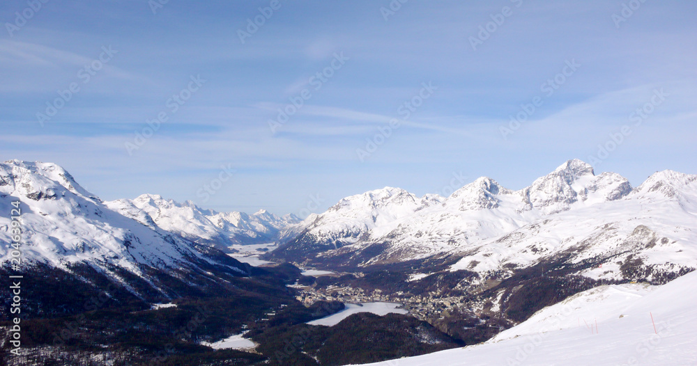 view of a winter landscape of the frozen lakes of the Engadin Valley and St. Moritz with the surrounding high alpine mountain peaks