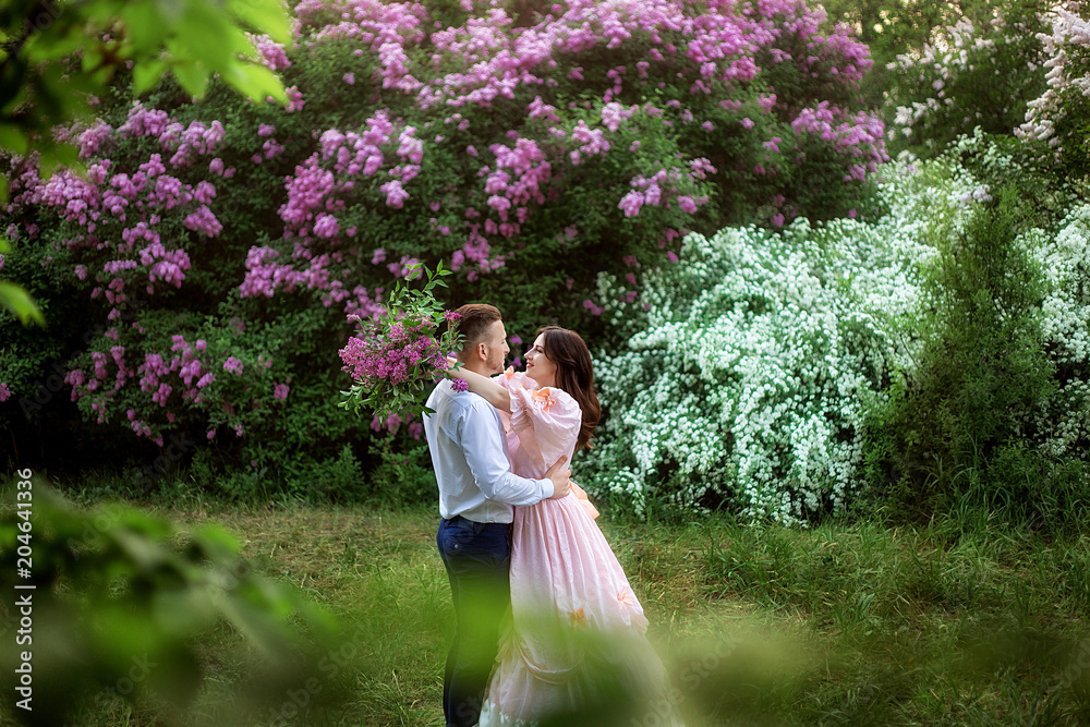 a loving couple in beautiful outfits against a background of blossoming lilac close-up