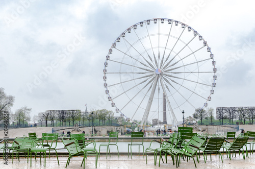 Green chairs on the Tuileries Gardens with the Roue de Paris in the background on a rainy day. Paris, France