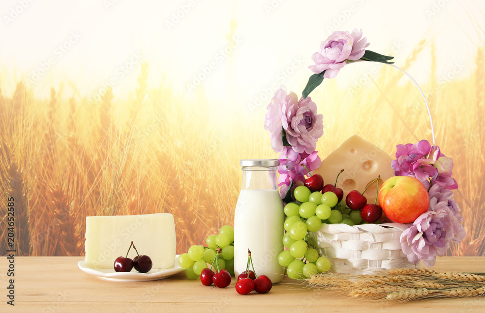 image of fruits and cheese in decorative basket with flowers over wooden table. Symbols of jewish holiday - Shavuot. image of fruits and cheese in decorative basket with flowers over wooden table. Symbols of jewish holiday - Shavuot.