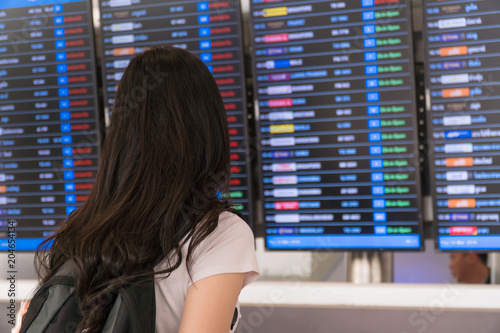 Tourist girl : She wearing casual clothes is posing at airport. She is checking the flight schedule of the airline she travels. Rear view. Copy space.
