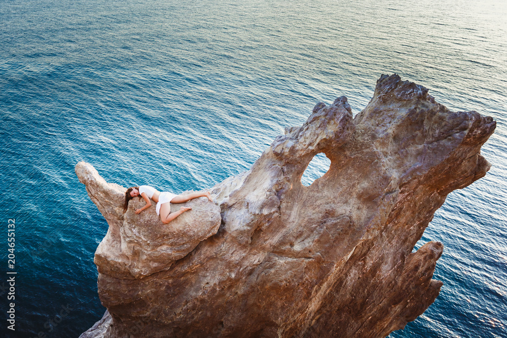 A high cliff in the form of a natural bed is high above the sea. The woman lies seductively on the top of the cliff, hand gracefully repeating the bends of the body. A rock in the shape of a crescent.