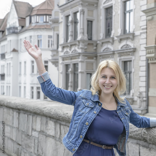 girl with blond hair and blue eyes is waving her hand in the old beautiful city.