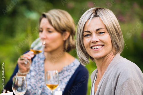 A group of friends gathered to share a meal around a table in the garden. Focus on a beautiful woman looking at the camera