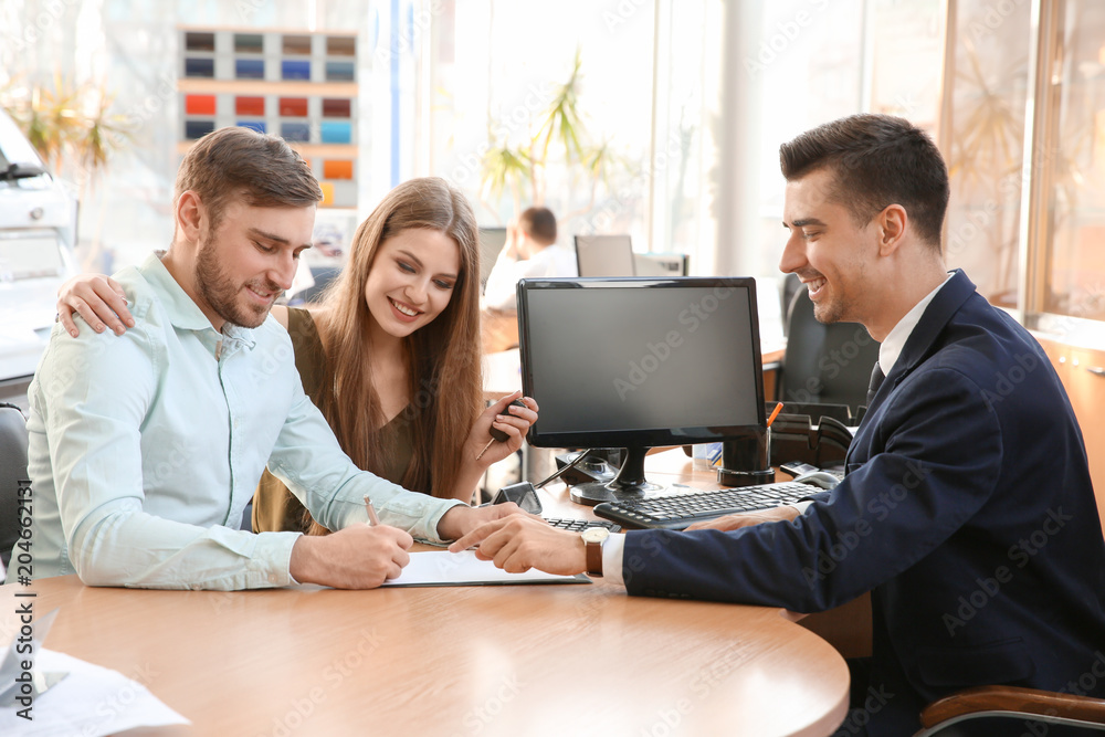 Fototapeta premium Young couple and salesman sitting at table in car salon. Buying auto