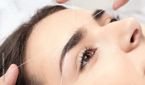 Photo Young woman having professional eyebrow correction procedure in beauty salon, cl