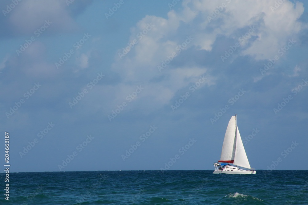 Sailboat on the Atlantic Ocean in Florida Frame Right in the Afternoon with Mostly Blue Sky and Some Clouds Overhead