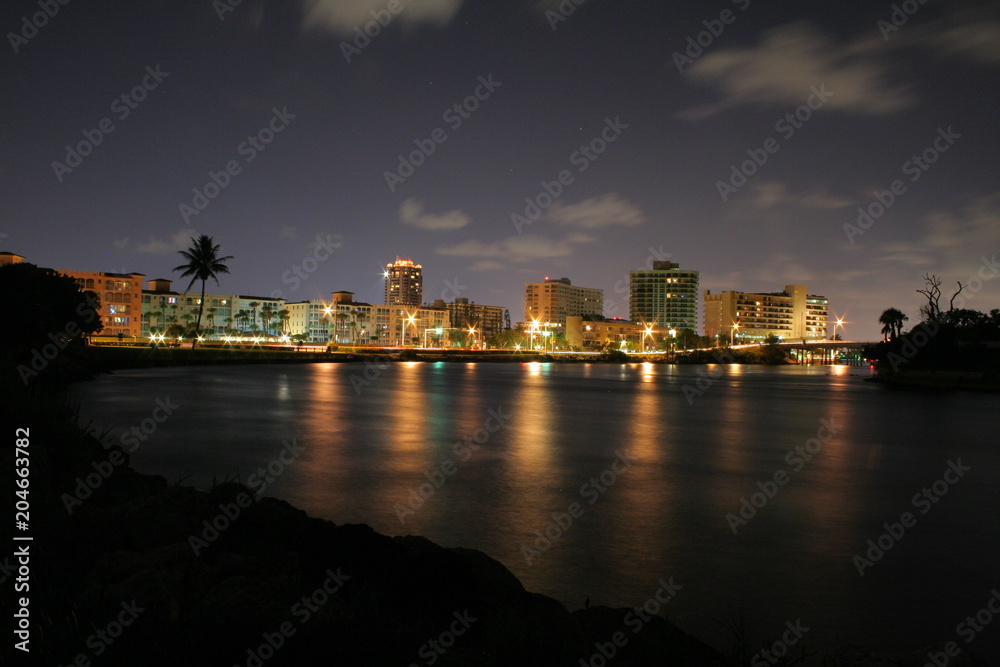 Looking Westwardly at the Boca Raton City Skyline from the Intracoastal Waterway at Camino Real and SR A1A at Night in a Long Time Exposure Creating Streaks of Car Headlights and Smooth Water