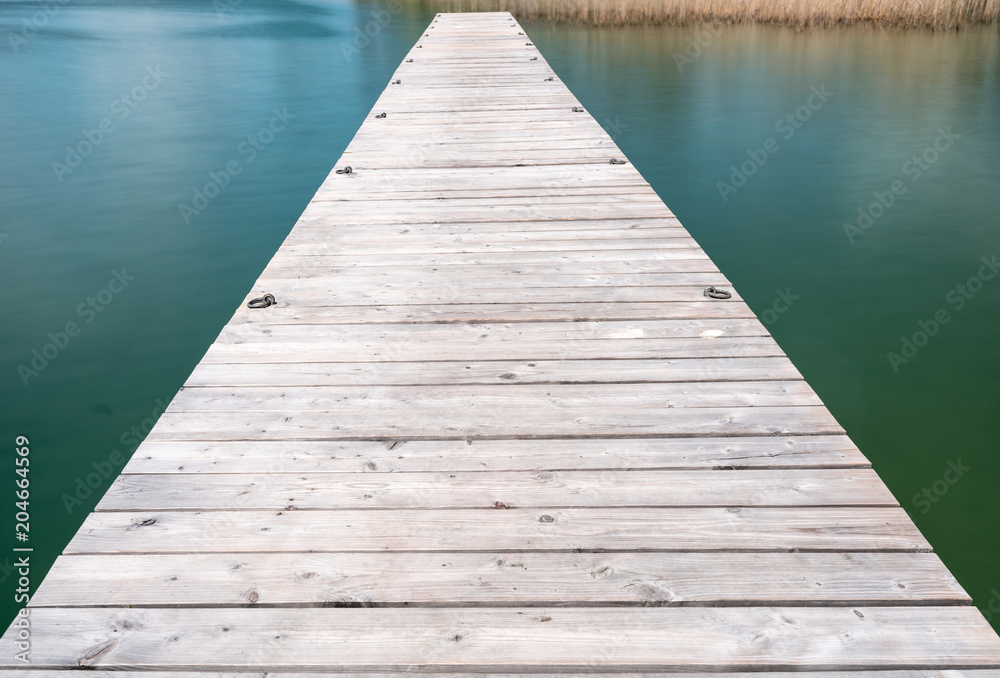 wooden pier jutting out into a turquoise and blue lake with golden reeds in the background wooden pier jutting out into a turquoise and blue lake with golden reeds in the background
