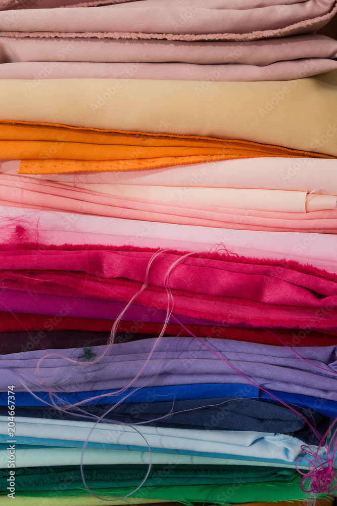 A pile of multicolored fabrics. Rainbow fabric background. Pile of bright folded fabric.