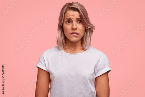 Portrait of discontent female curves lips, feels nervous before making inportant decision, has frustrated expression, wears casual white t shirt. People, emotions, facial exressions concept.