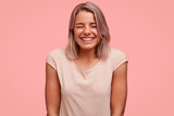 Positive European female laughs joyfully, listens funny joke, has broad smile, demonstrates teeth with braces, isolated over pink background. Optimistic overjoyed woman with bobbed hairstyle
