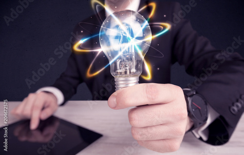 A classy businessman holding a colorful light bulb with shining circles in front of dark background concept.