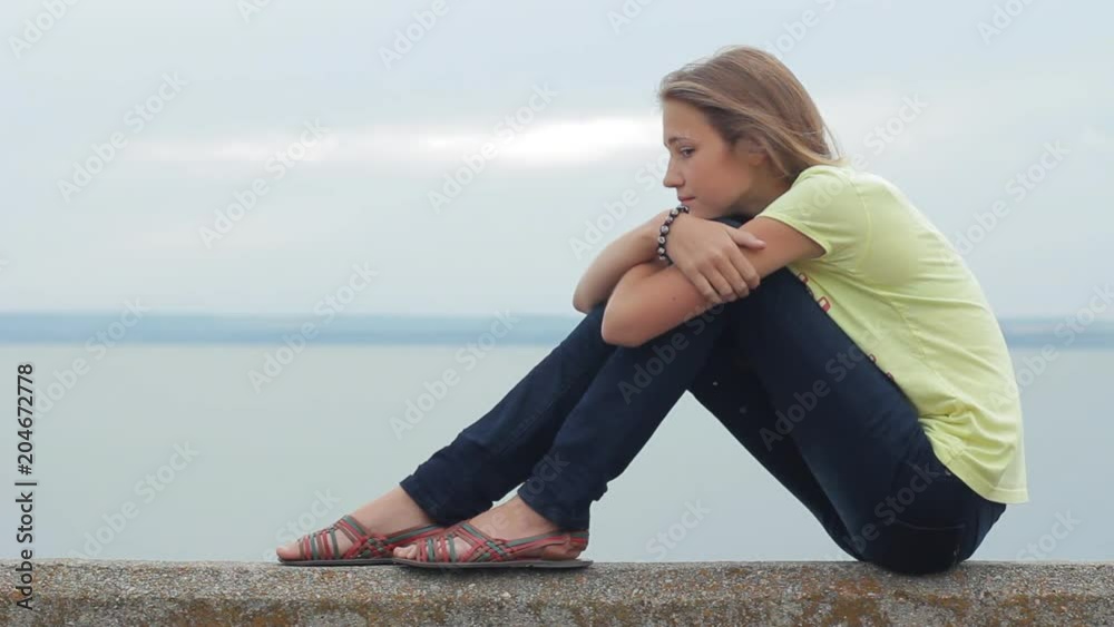 Teenager girl alone sitting sitting hugging her knees on beach in evening