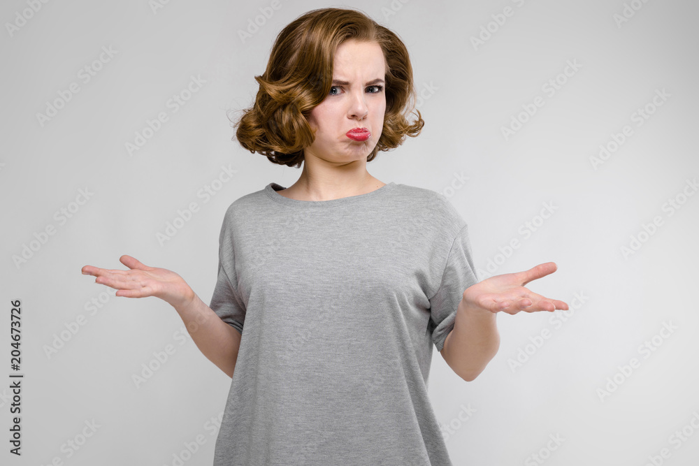 Charming young girl in a gray T-shirt on a gray background. The girl spread her arms Charming young girl in a gray T-shirt on a gray background. The girl spread her arms