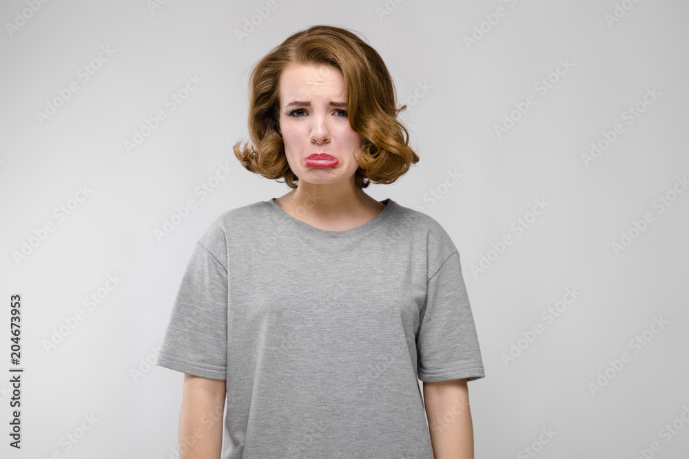 Charming young girl in a gray T-shirt on a gray background. The girl is ready to burst into tears Charming young girl in a gray T-shirt on a gray background. The girl is ready to burst into tears