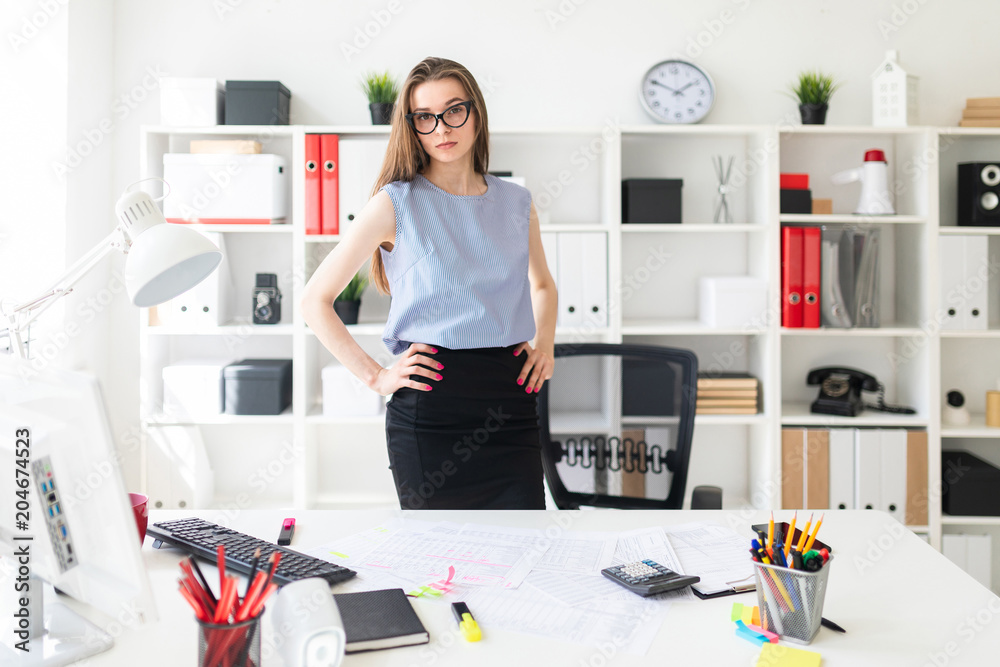 Beautiful Young girl in the office is standing near the table and put her hands on her hips. Beautiful Young girl in the office is standing near the table and put her hands on her hips.