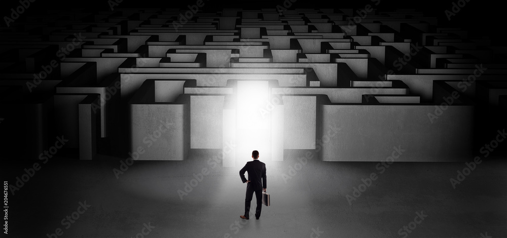 Lost businessman standing at the dark labyrinth with illuminated door
Lost businessman standing at the dark labyrinth with illuminated door