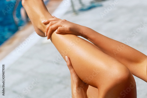Women's beautiful sexy legs.Sunbath protection.Woman rubbing sunblock on her leg..Woman applying sunscreen creme.