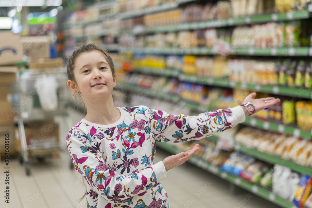 Cheerful girl in a supermarket shows on products. A girl of 8 years in a supermarket