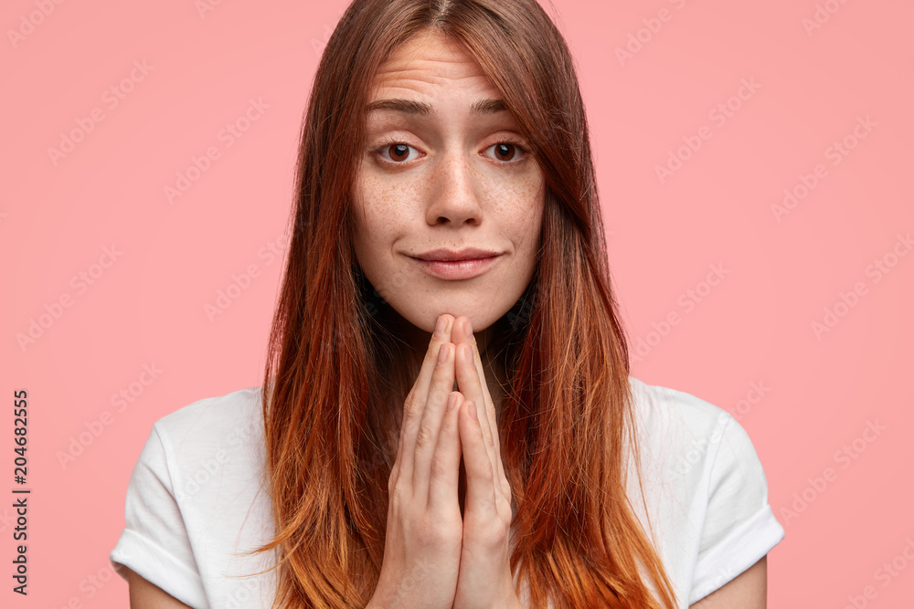 Close up portrait of pleading female has freckled face, looks with big hope at camera, keeps palms together, asks for forgiveness as betrayed boyfriend, feels guilty. Helpless young woman prays Close up portrait of pleading female has freckled face, looks with big hope at camera, keeps palms together, asks for forgiveness as betrayed boyfriend, feels guilty. Helpless young woman prays