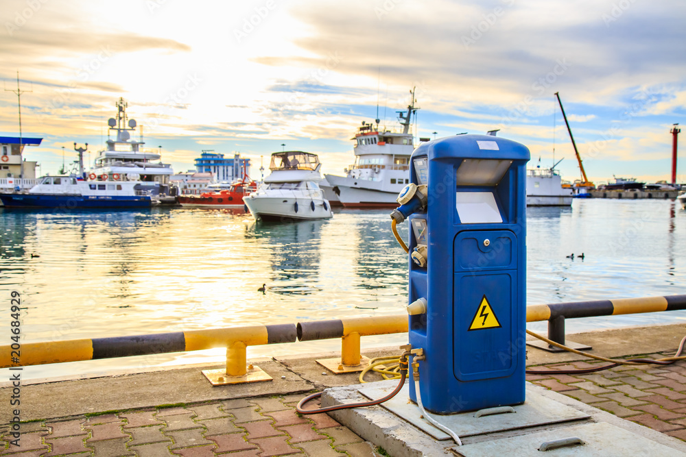 Charging station for boats, electrical outlets to charge ships in harbor -  supply electricity for recharging of battery on shore in marina jetty.  Luxury yachts docked in port at sunset. Photos