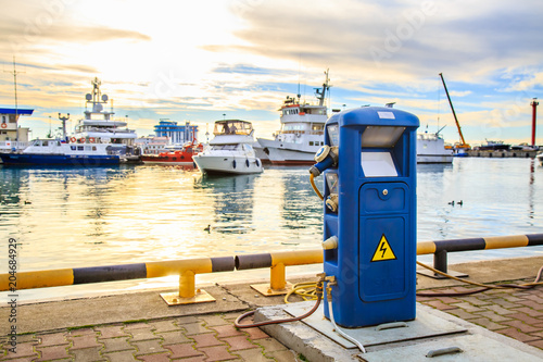 Charging station for boats, electrical outlets to charge ships in harbor - supply electricity for recharging of battery on shore in marina jetty. Luxury yachts docked in port at sunset.