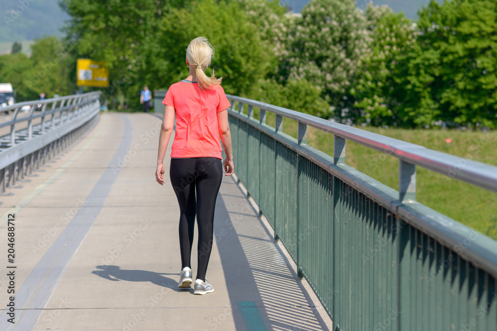 Blond woman jogging across a pedestrian bridge Blond woman jogging across a pedestrian bridge
