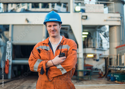 Marine Deck Officer or Chief mate on deck of offshore vessel or ship , wearing PPE personal protective equipment - helmet, coverall. He speaks to VHF walkie-talkie radio photo