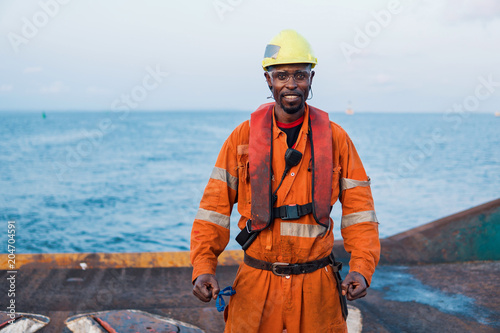 Seaman AB or Bosun on deck of offshore vessel or ship , wearing PPE personal protective equipment - helmet, coverall, lifejacket, goggles. He is happy of his job photo