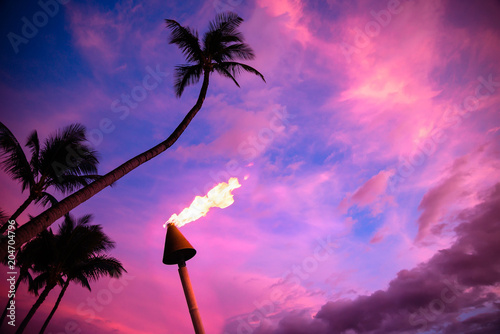 Tiki torch against colorful tropical sunset with palm trees
