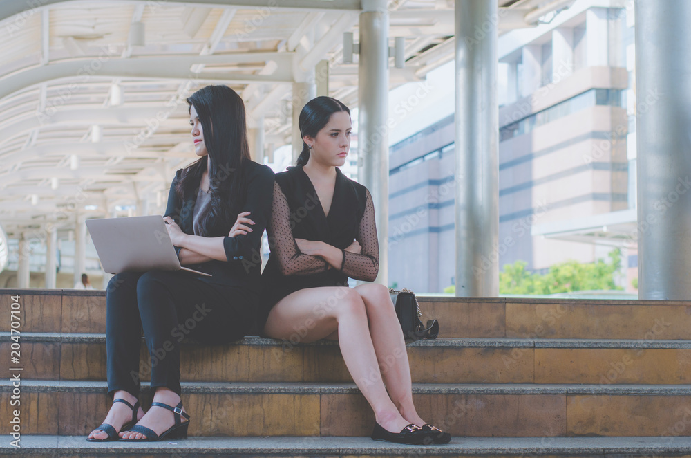 two business woman touchy and angry and stressed at outdoor sitting on concrete stair in city with using laptop checking about lose business planning project.