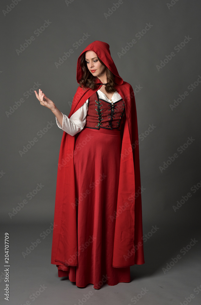 full length portrait of woman wearing red fantasy costume with cloak, standing pose on grey studio background. full length portrait of woman wearing red fantasy costume with cloak, standing pose on grey studio background.