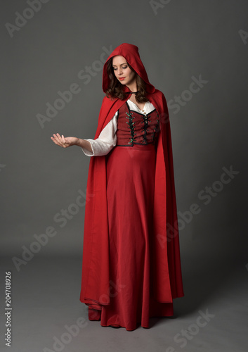 full length portrait of woman wearing red fantasy costume with cloak, standing pose on grey studio background.