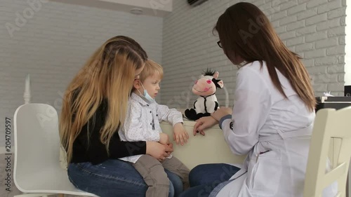 Female pediatrician talking to young child and mother on inspection in the clinic. Mother and son visiting pediatrician. The doctor plays with the baby and with the toy. photo