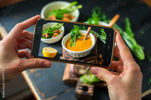 Phone photography of food. Woman hands take photo of lunch with smartphone for social media. Pumpkin soup. Raw vegan vegetarian healthy dinner 