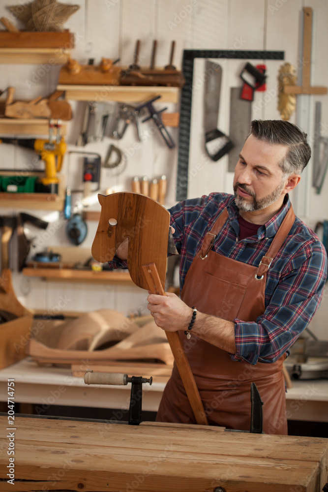 A Wooden Horse is a Toy for All Time. Carpenter works with a planer in a workshop for the production of vintage furniture. He makes wooden horse for his grandson