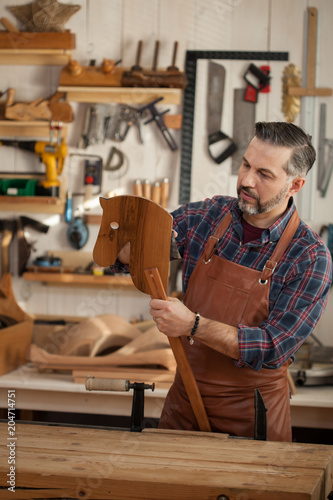 A Wooden Horse is a Toy for All Time. Carpenter works with a planer in a workshop for the production of vintage furniture. He makes wooden horse for his grandson