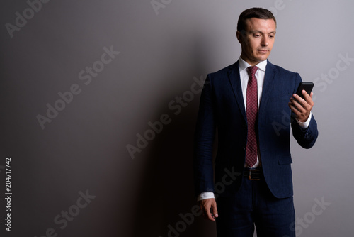 Businessman wearing suit while using mobile phone against gray b
