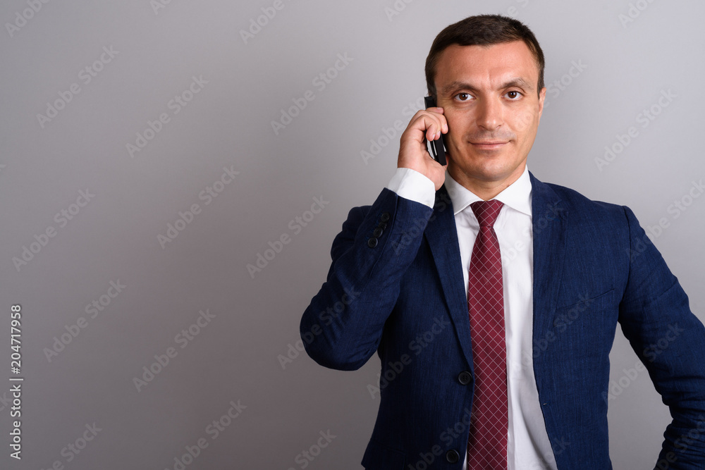 Businessman wearing suit while using mobile phone against gray b Businessman wearing suit while using mobile phone against gray b