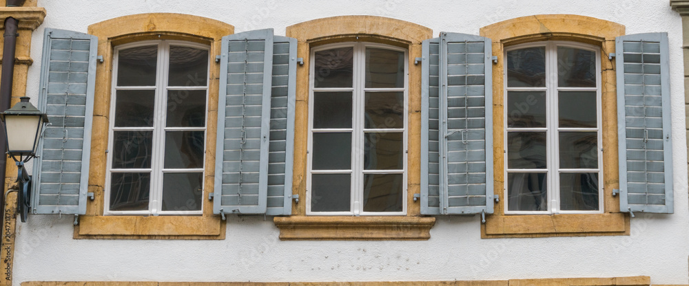 close up view of three windowls with wooden window shutters in blue